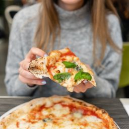 Portrait of young woman eating pizza. Neapolitan pizza from wood-burning stove. lunch in an Italian restaurant. Table near to a large window. Margarita and four cheese